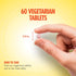 A hand holds a small, round vegetarian tablet, measuring 1/4 inch in diameter.